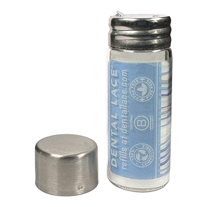 Cylindrical glass floss container with a metallic cap and waves ‘Dental Lace’ label on a white background.