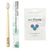 A bamboo  toothbrush with a light wood handle and white bristles, shown next to its white packaging sleeve and a white unpaste toothpaste pouch on a plain white background.