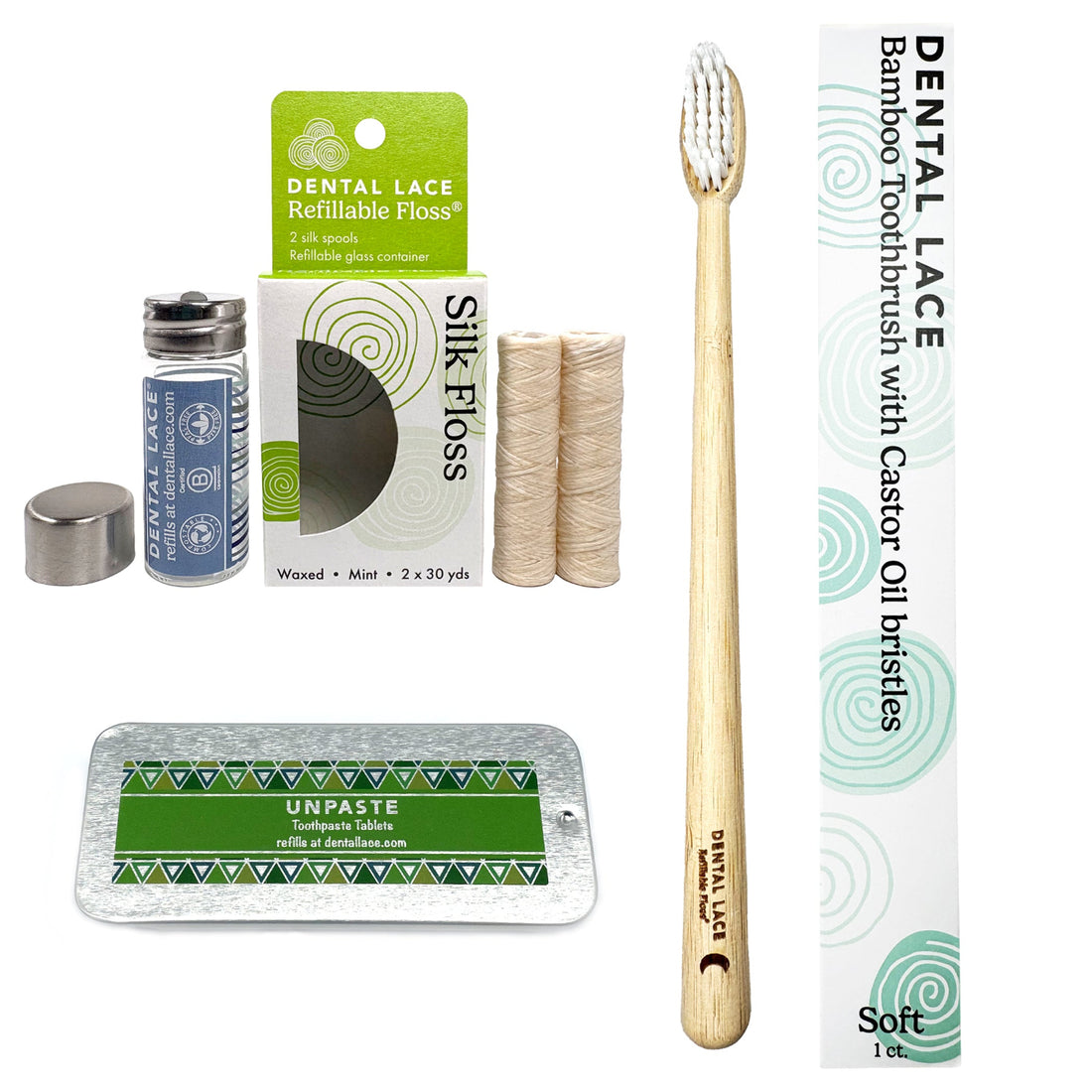 A bamboo toothbrush with a light wood handle and white bristles stands upright next to its white and green branded box. Surrounding it are included accessories: a small glass bottle of dental lace refill, a metal cap, two silk floss spools, and a silver tray with a green Unpaste toothpaste tablet packet.