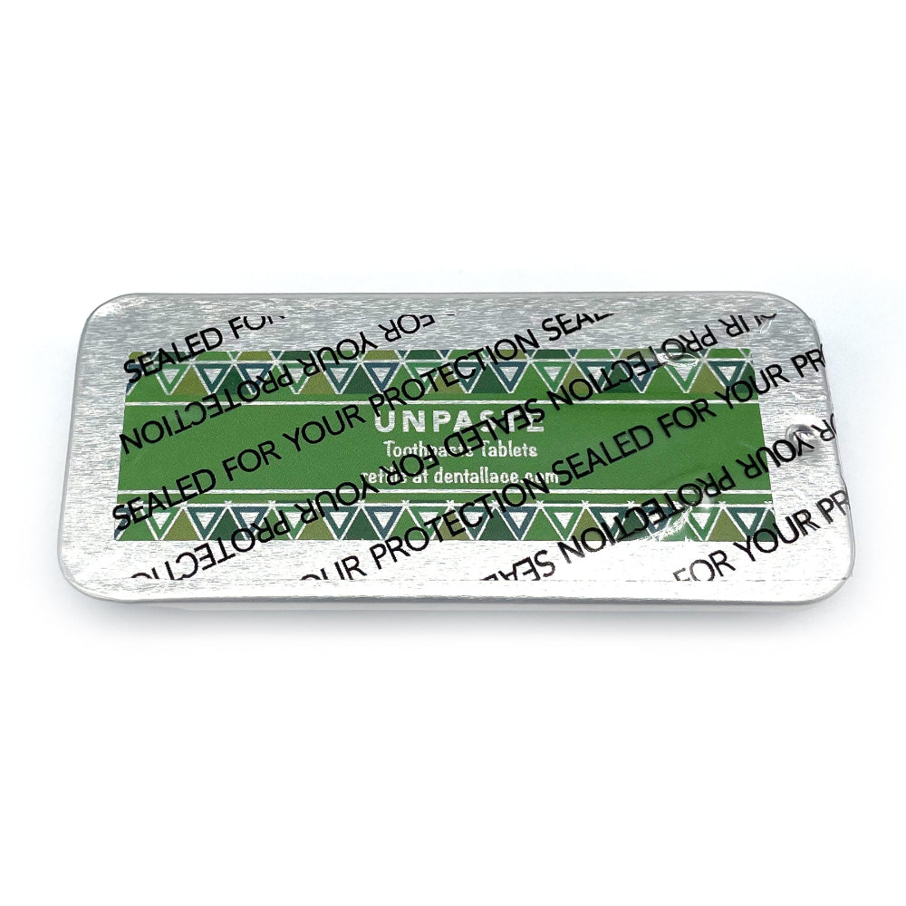 Metallic tin with unpaste fluoride free toothpaste tablets and a green design on a white background.