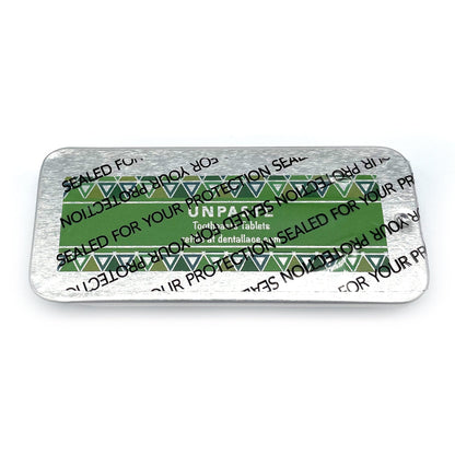 Metallic tin with unpaste fluoride free toothpaste tablets and a green design on a white background.